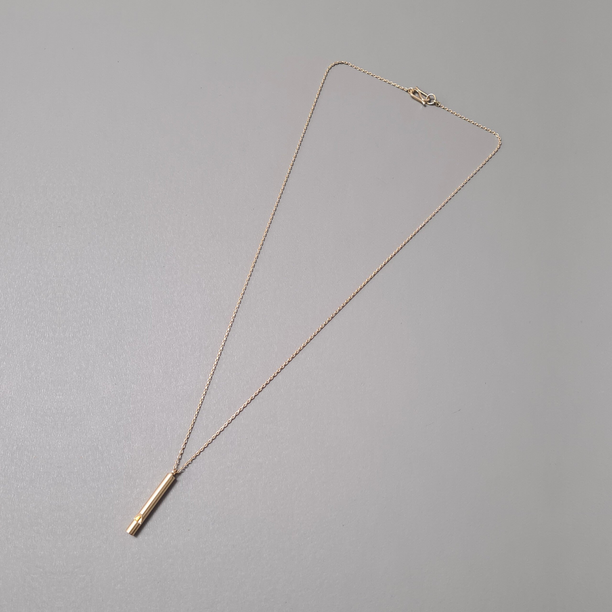 Gold whistle necklace flat lay on grey background.