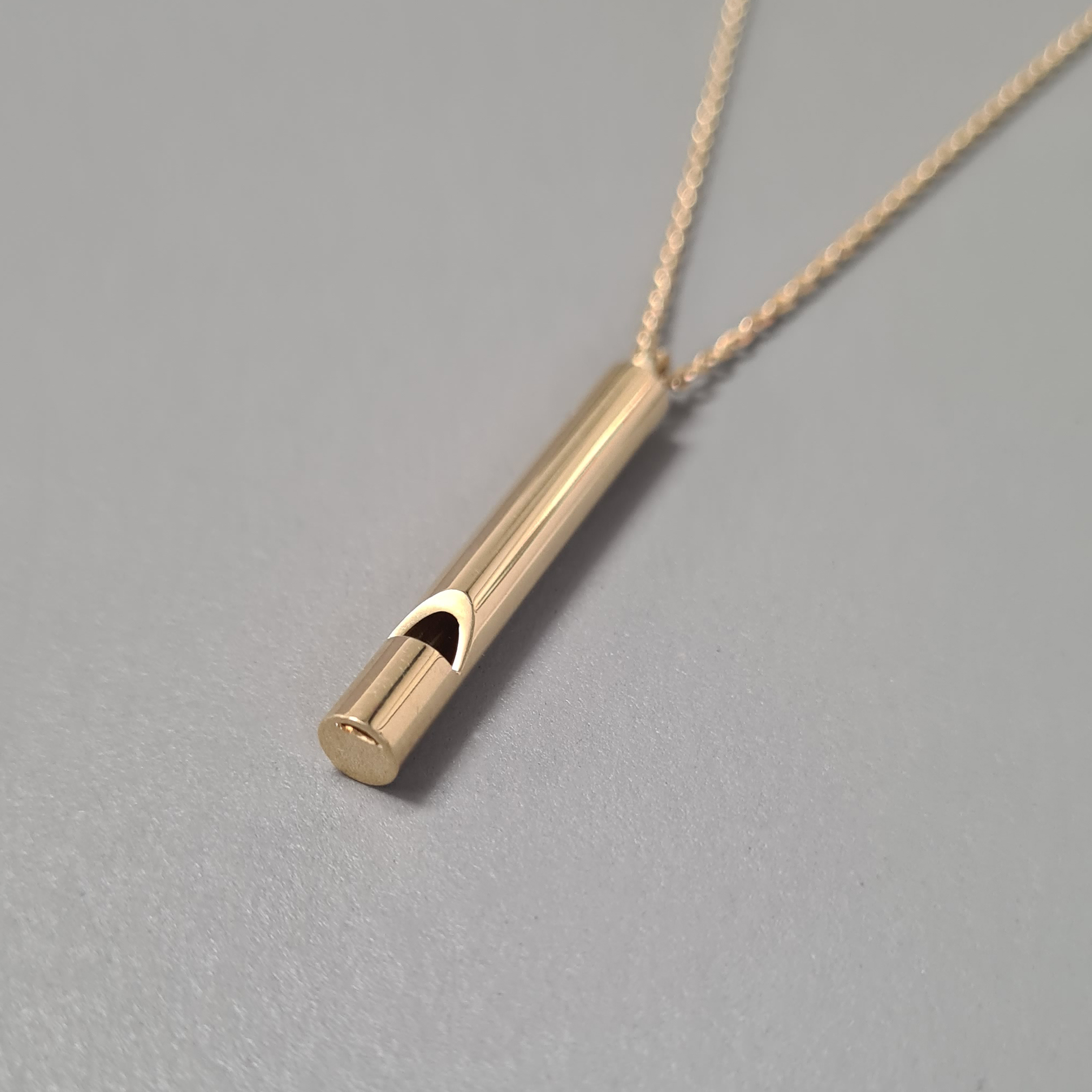 Close up of 18k gold whistle on grey background.