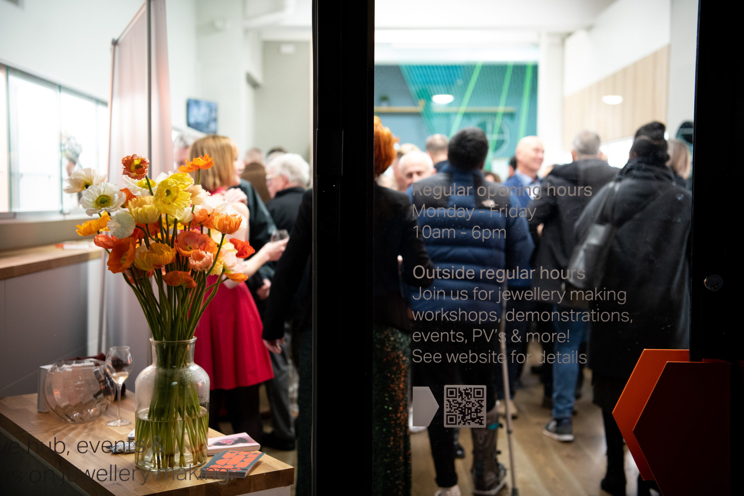 people gathered in jewellery exhbition space, seen through glass window, with a vase of flowers