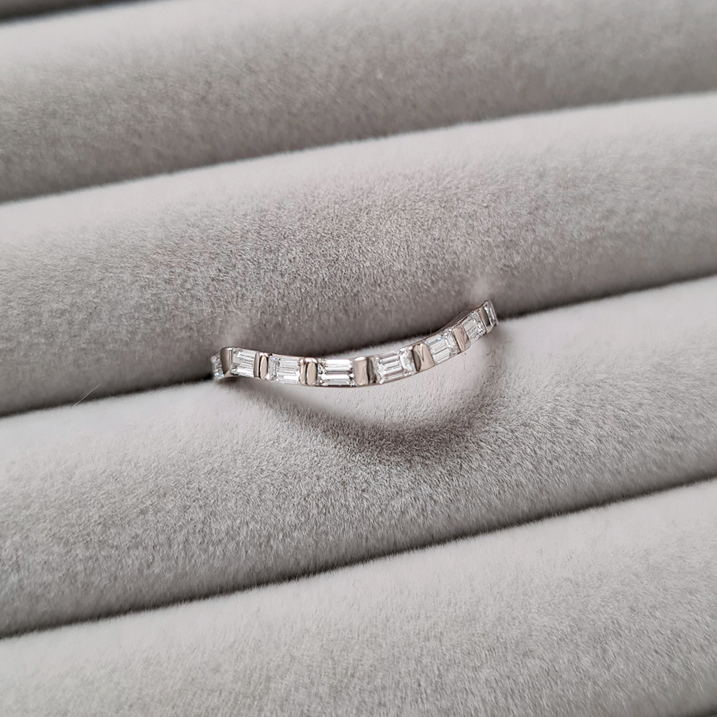 18k white gold 'wave' shaped eternity wedding ring set with baguette diamonds on a grey velvet tray.