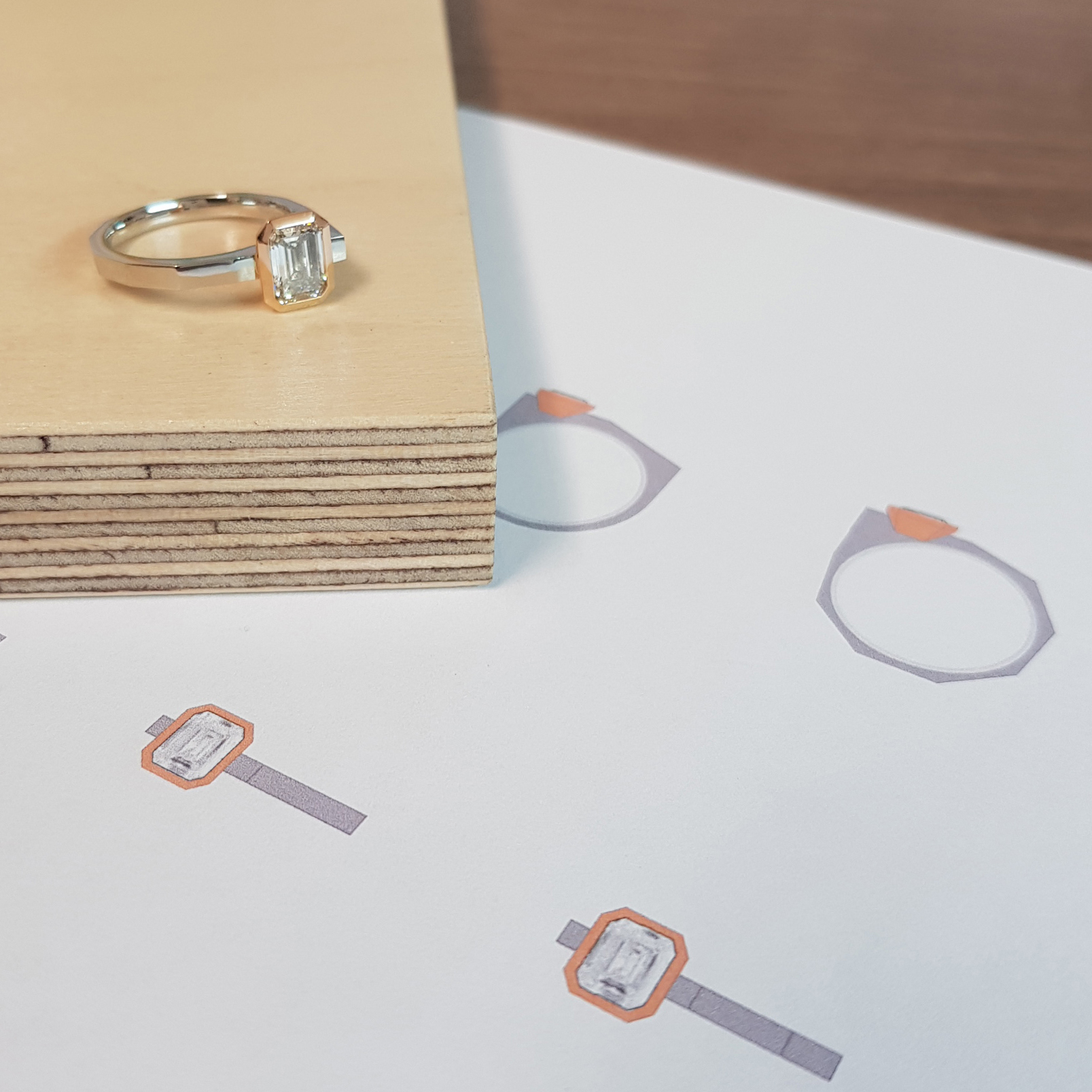 diamond engagement ring with diamond set in rose gold on a platinum band on wooden blaock over computer drawings of design