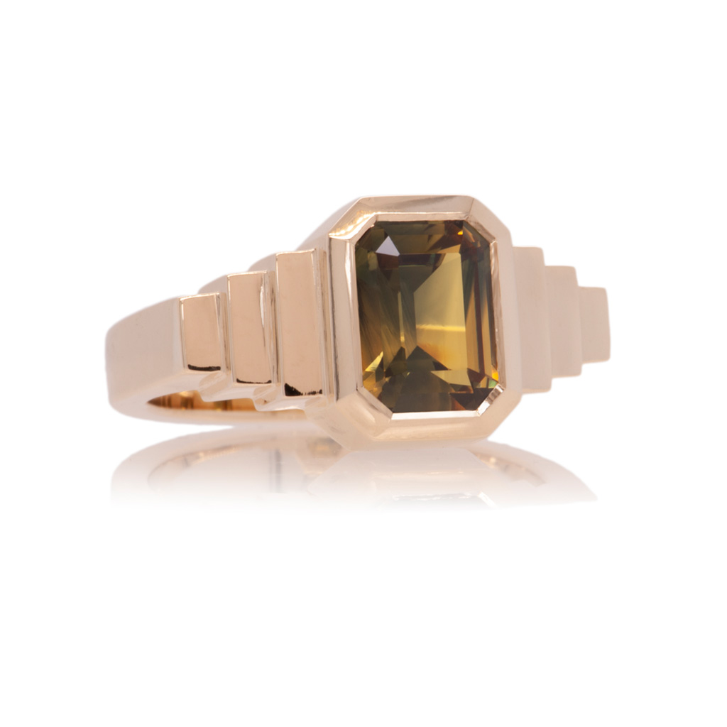 Ring with 3no stepped shoulders either side of a stepped cut yellow green sapphire. The ring is lying down and on a white background.