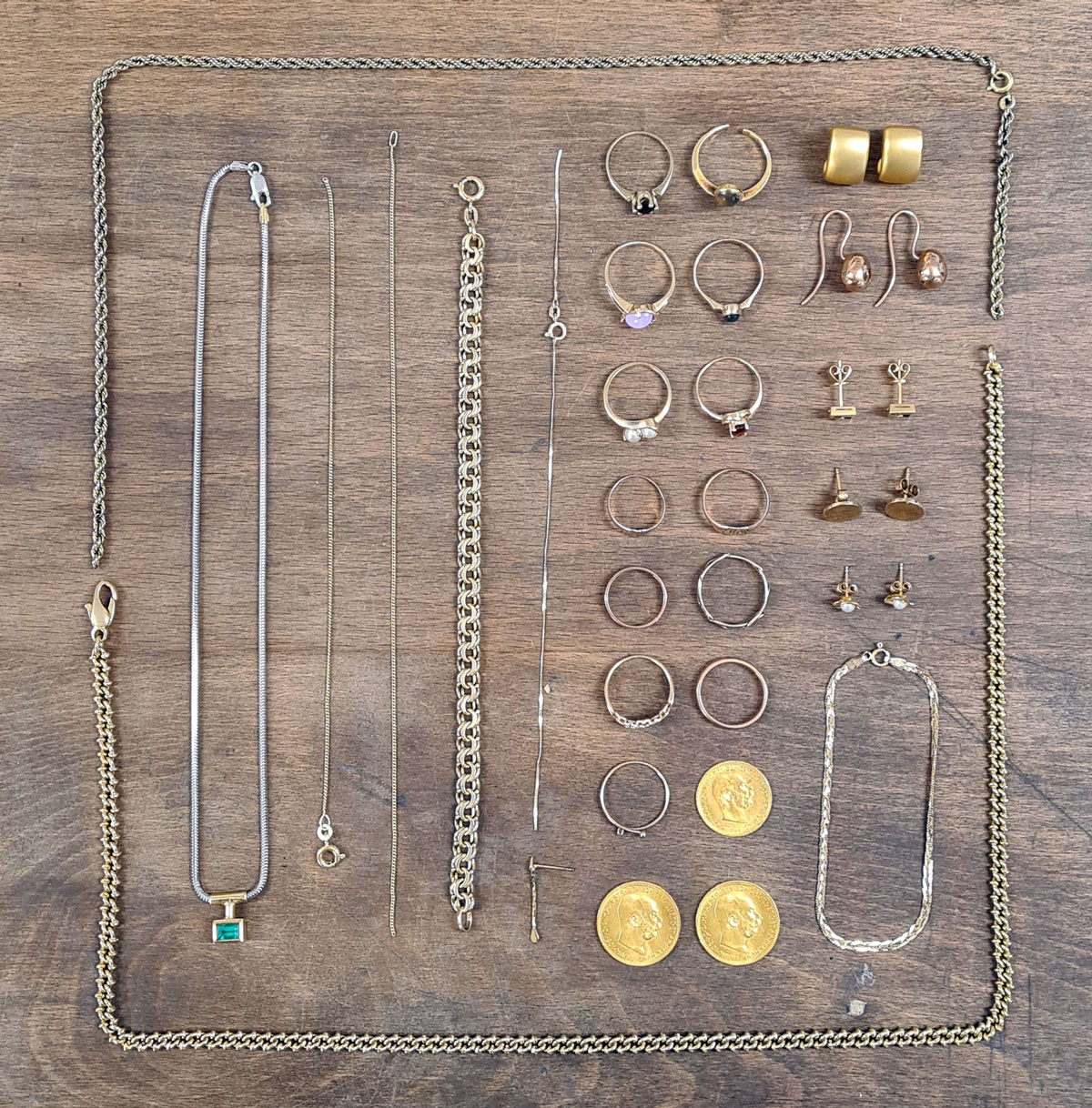 Flat lay of gold chain, earrings, bracelets and coins on a wooden bench.