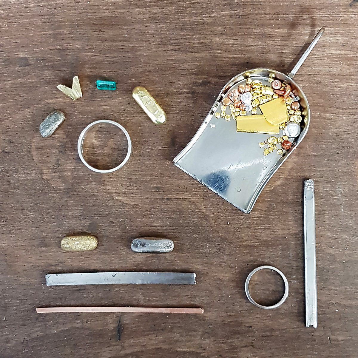 Flat lay of raw materials (gold and gemstones) and semi-worked pieces on Amanda timber workbench.