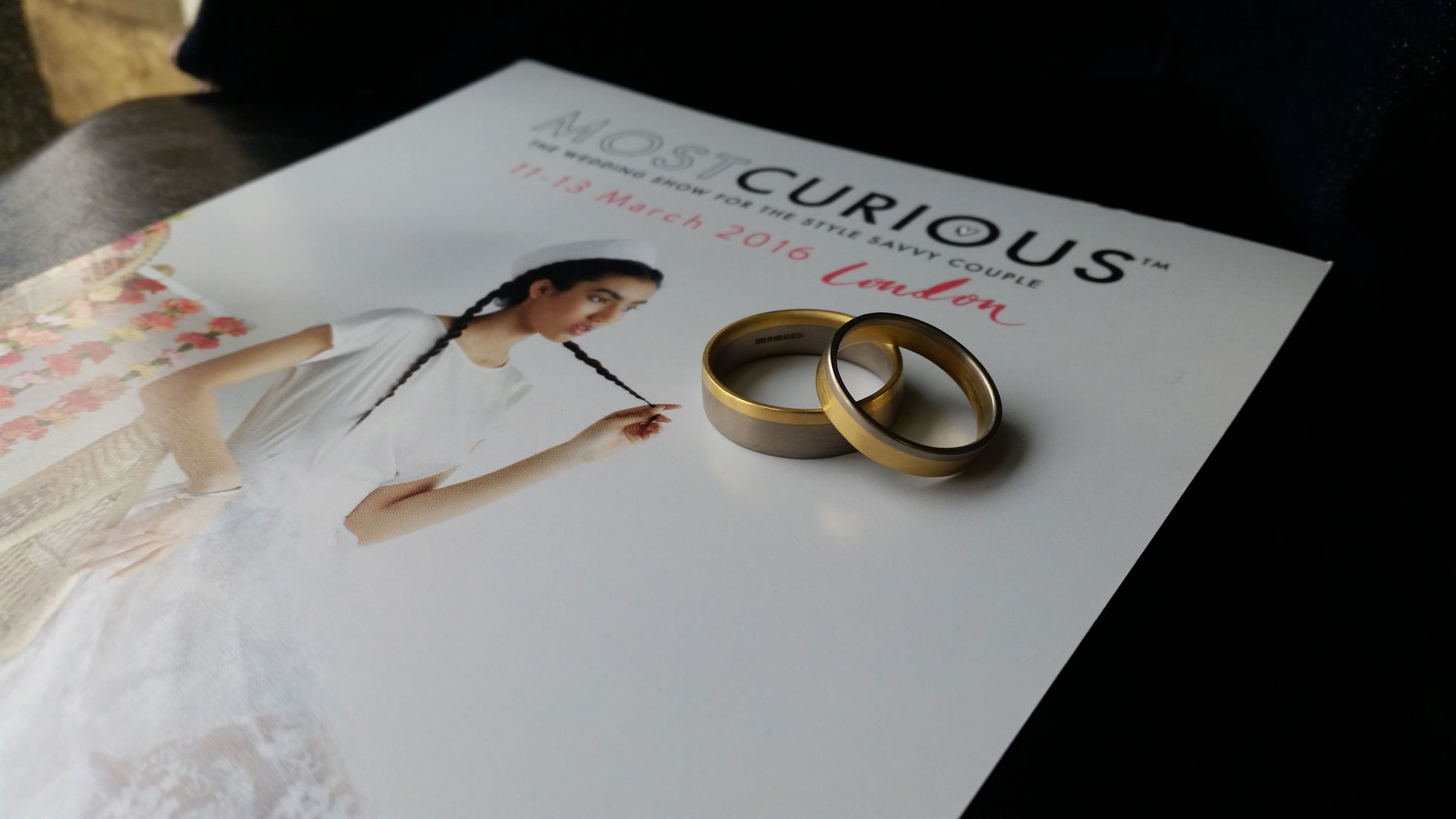 Most Curious Wedding Fair flyer from 2016 with Amanda's two tone Fairtrade Gold wedding rings on top.
