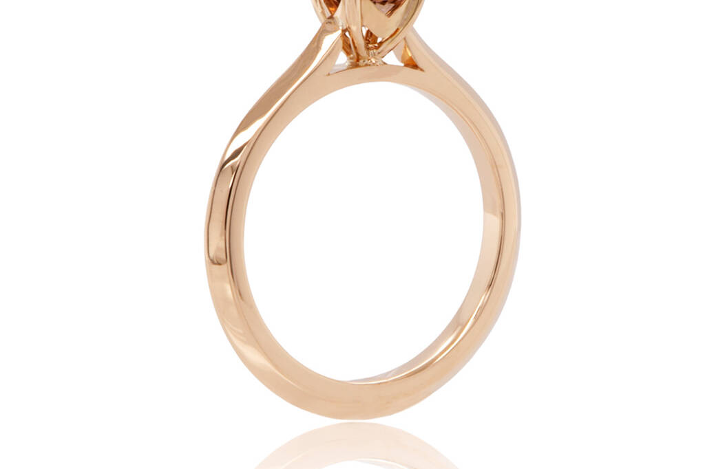 Solitaire engagemet ring in yellow gold holding a round champagne diamond standing upright on a white background.