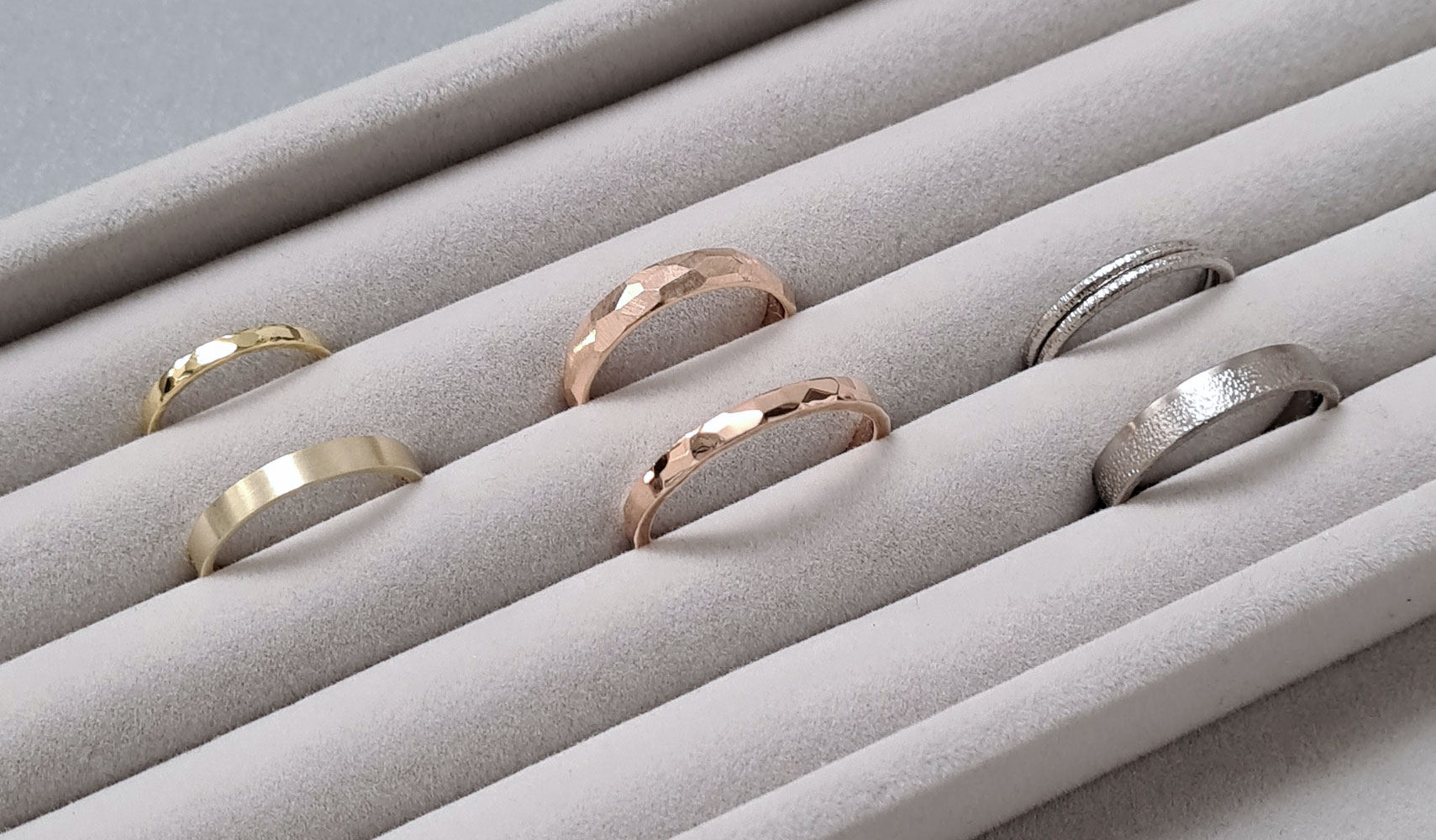 Three pairs of wedding rings with different textures on a grey velvet tray.