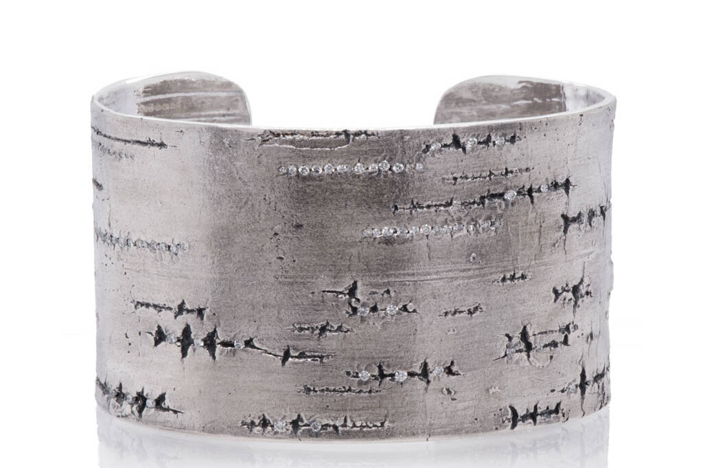 Silver cuff bracelet with lined texture of silver birch embedded with diamonds against a white background.