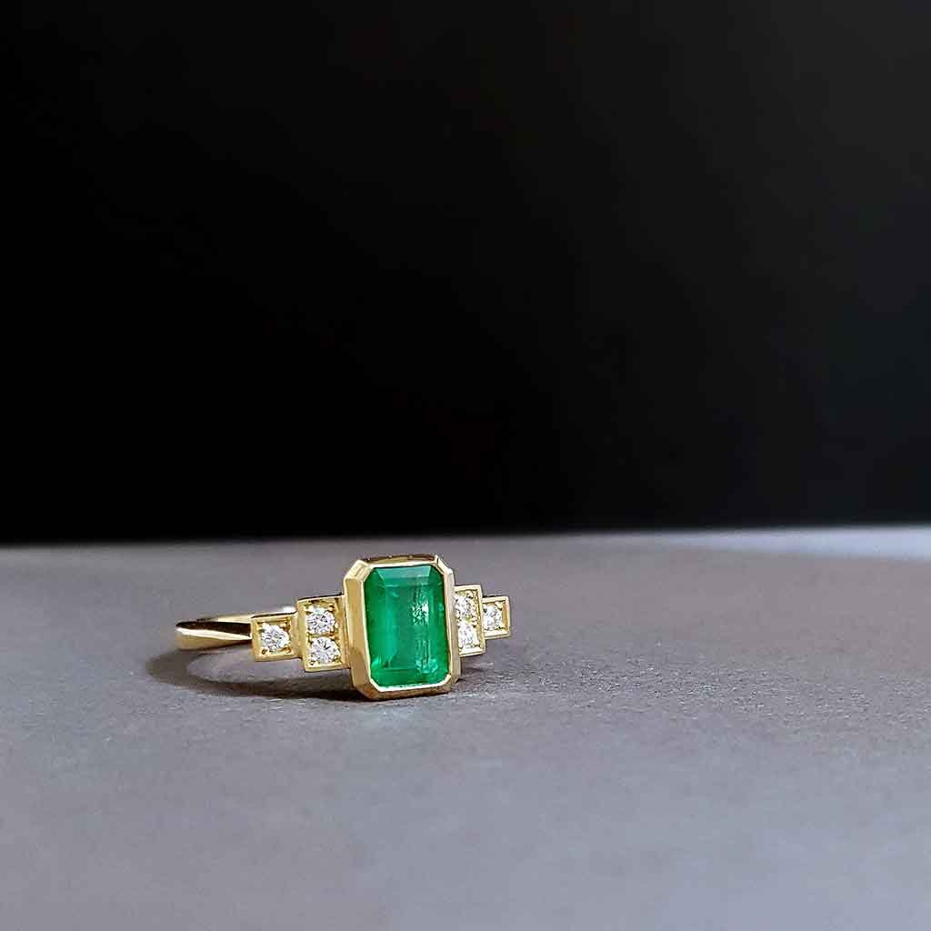 gold and emerald engagement ring in art deco style on grey background