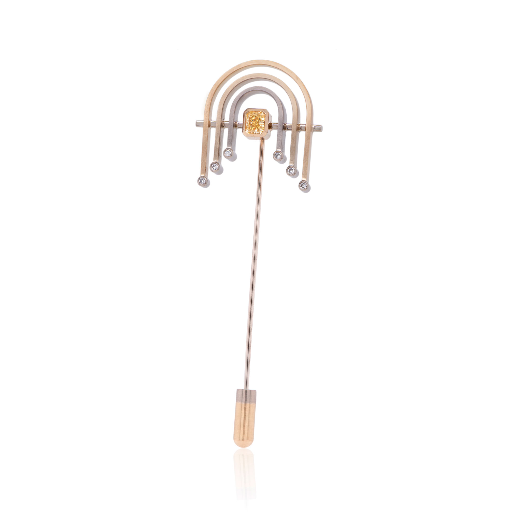 A lapel pin featuring a radiant cut yellow diamond and three gold arches radiating outwards. Small diamonds punctuate the ends of the arches on either side. The pin is positioned vertically on a white background.