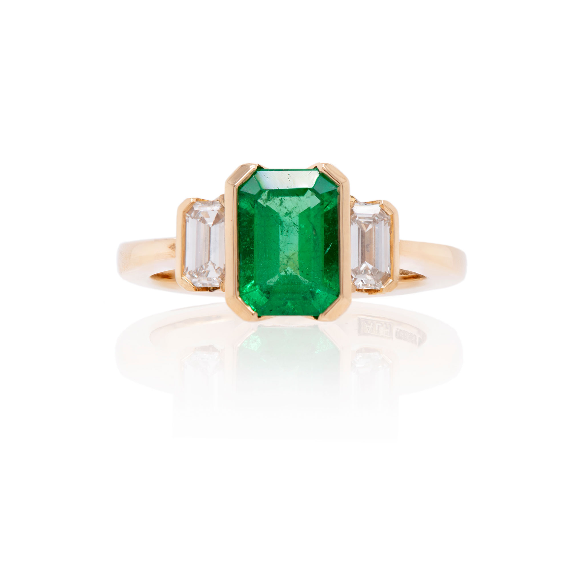Yellow gold emerald and baguette diamond engagement ring on a white background